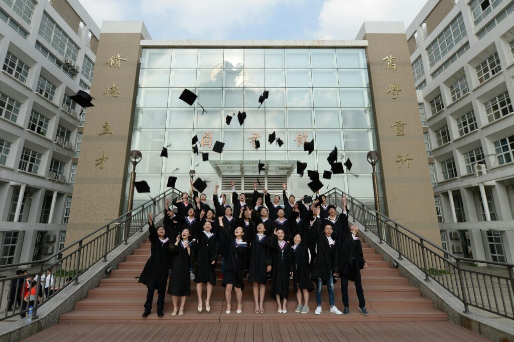 Group of students celebrating graduation by tossing caps in the air outside a school building.